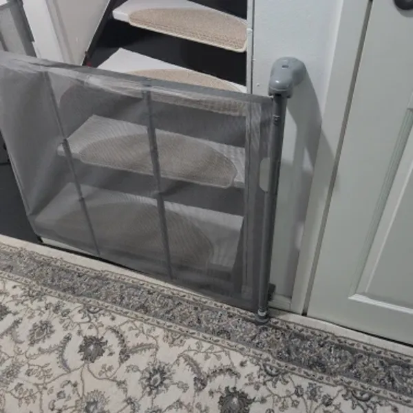 Gray SnugGate mesh baby gate installed at the bottom of an interior staircase on a rug