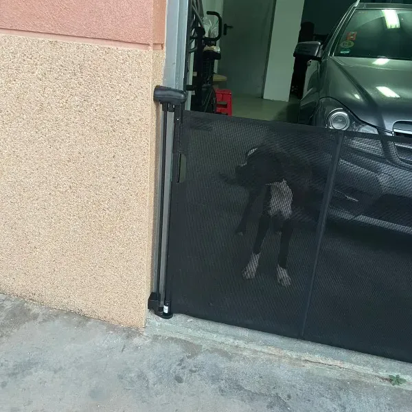 Black SnugGate mesh baby gate installed in front of a garage, with a dog visible behind the gate