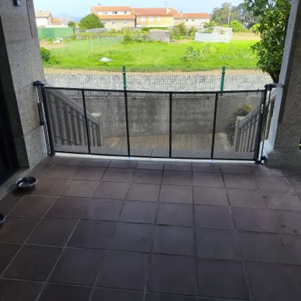 Gray SnugGate mesh baby gate installed on an outdoor terrace, with a pet food bowl visible on the floor